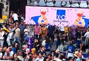 Een grote menigte op een bruisend festival, met een digitaal scherm waarop badeendjes en het X²O badkamers-logo te zien zijn.